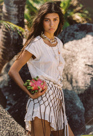 A woman outdoors wearing a white short-sleeve top and a white skirt with a black geometric lattice pattern