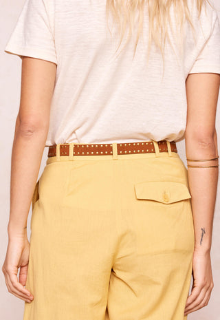A person shown from the back wearing a cream short-sleeve t-shirt, a brown studded belt, and mustard yellow trousers with a flap pocket.