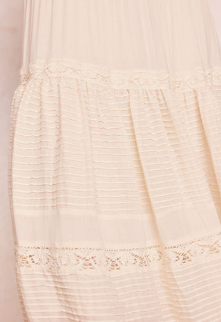 Close-up of a cream-colored sheer tulle dress with horizontal pleated detailing and delicate lace trim.