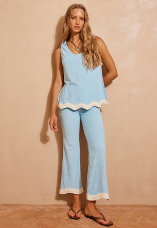 a-woman-modeling-a-light-blue-two-piece-lounge-set-with-white-contrast-trim-consisting-of-a-sleeveless-top-and-matching-cropped-pants-standing-against-a-textured-beige-wall
